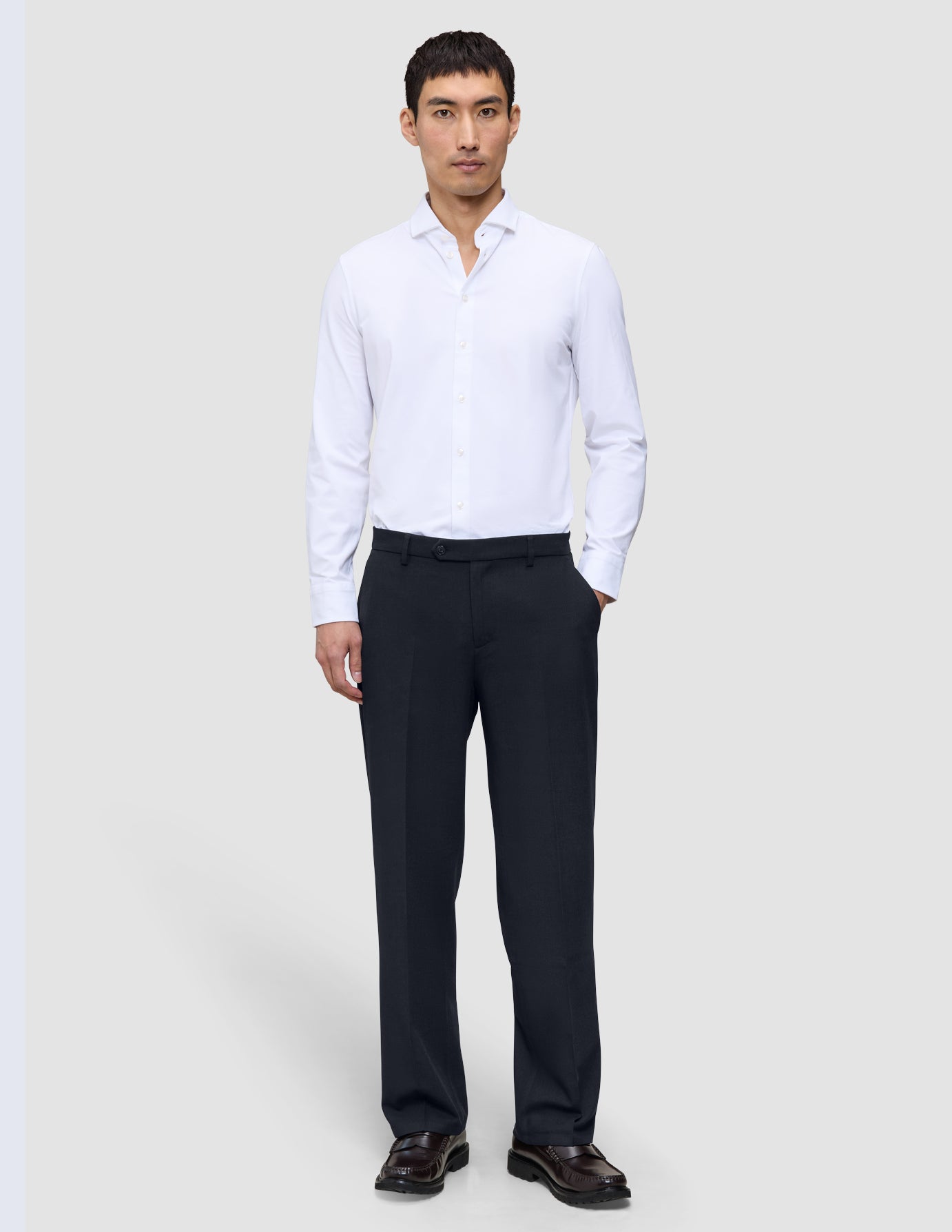 Ein Mann, der ein weißes Hemd und eine dunkelblaue Motion Suit-Hose im Relaxed-Schnitt in der Farbe Midnight Blue trägt.
